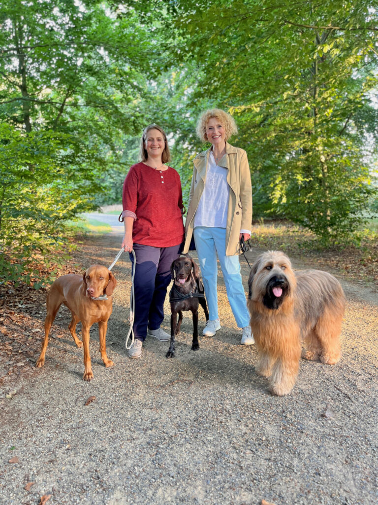 zwei Trainer lächeln mit ihren Hunden an der Leine in die Kamera
