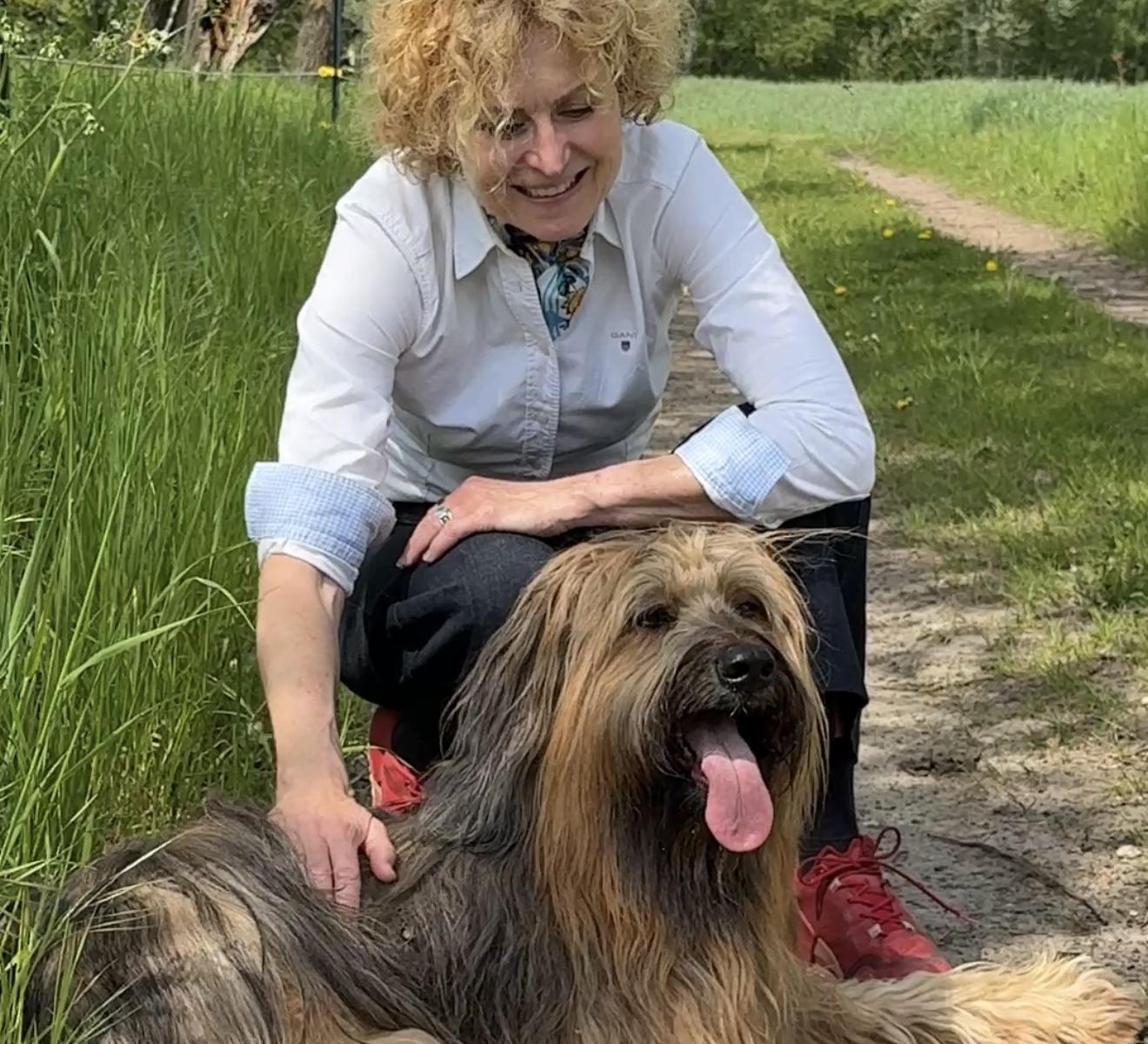 Eine Frau mit Hund kniet hinter ihrem Hund, der auf dem Boden liegt. Sie streichelt ihn und lächelt.