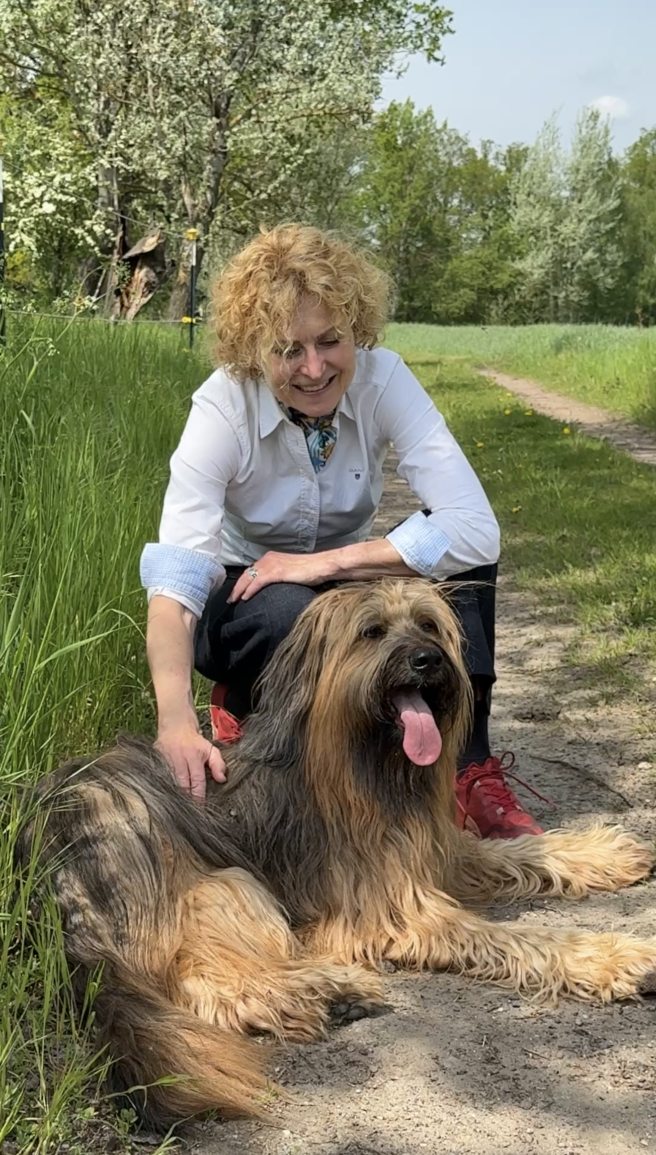 Eine Frau mit Hund kniet hinter ihrem Hund, der auf dem Boden liegt. Sie streichelt ihn und lächelt.