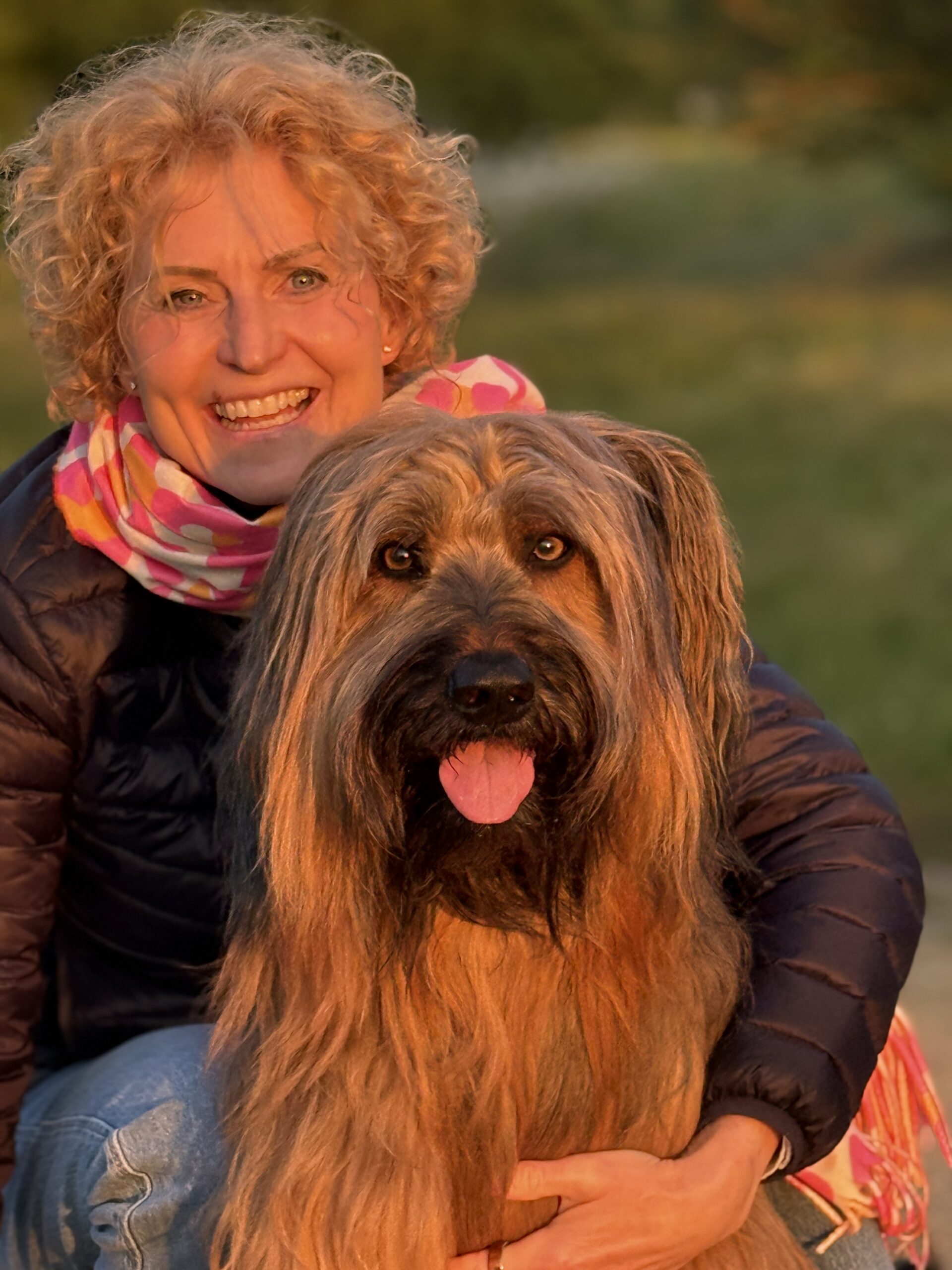 Eine Frau hockt hinter ihrem Hund in der Abendsonne und hat sich das Leben mit Hund genau so vorgestellt.
