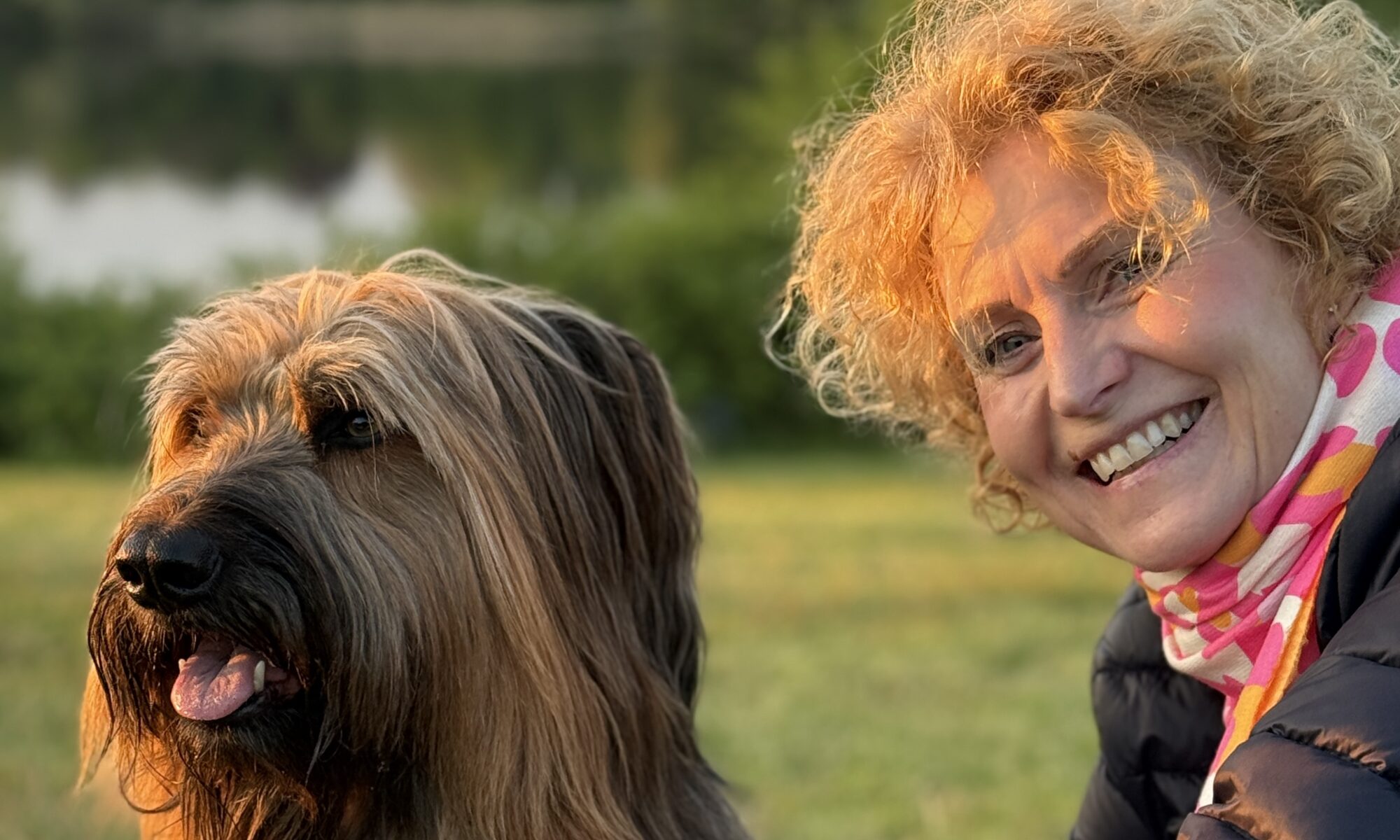 Eine Frau hockt entspannt und befreit hinter ihrem Hund in der Abendsonne und hat sich das Leben mit Hund genau so vorgestellt.
