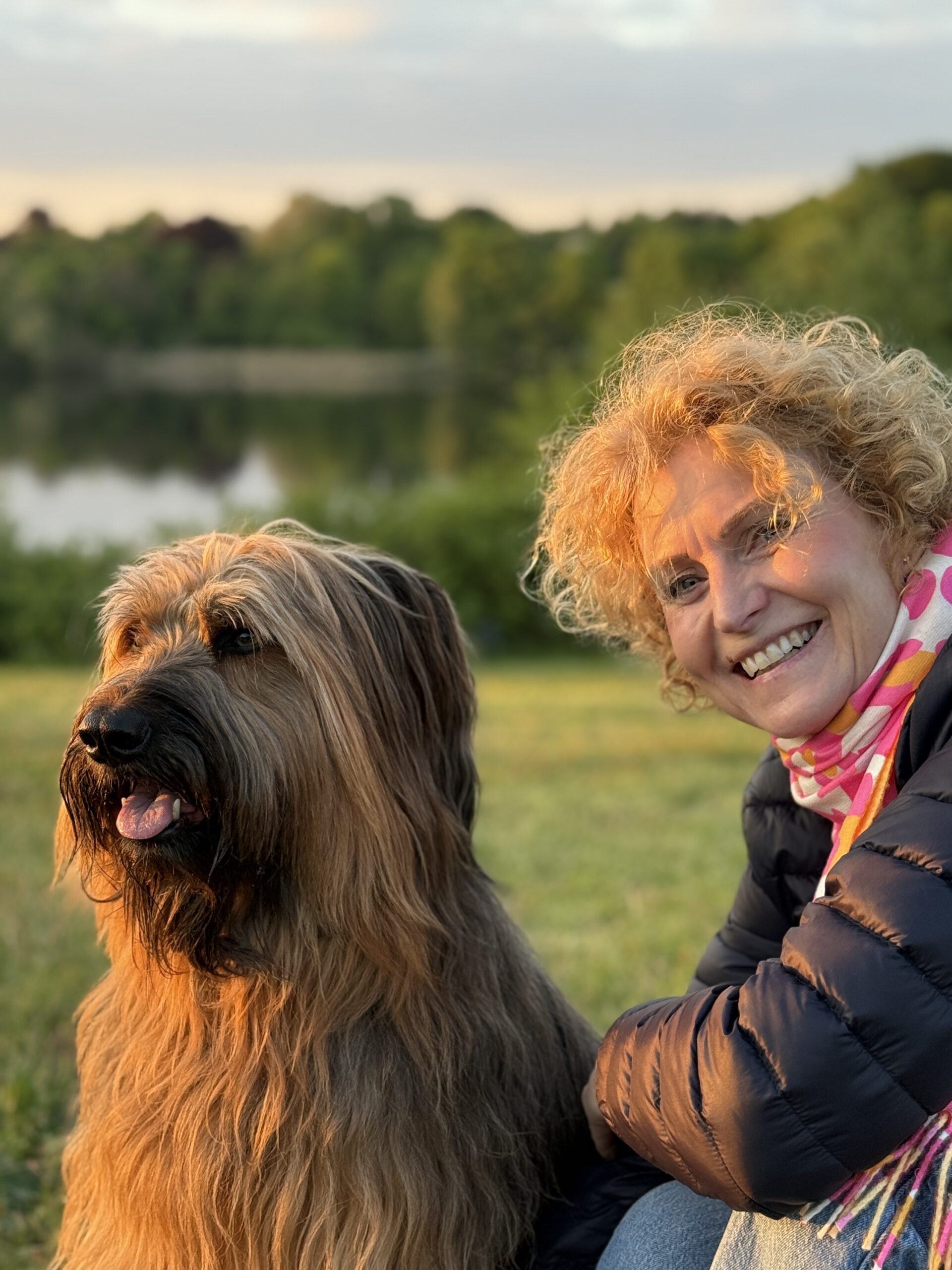 Eine Frau hockt entspannt und befreit hinter ihrem Hund in der Abendsonne und hat sich das Leben mit Hund genau so vorgestellt.