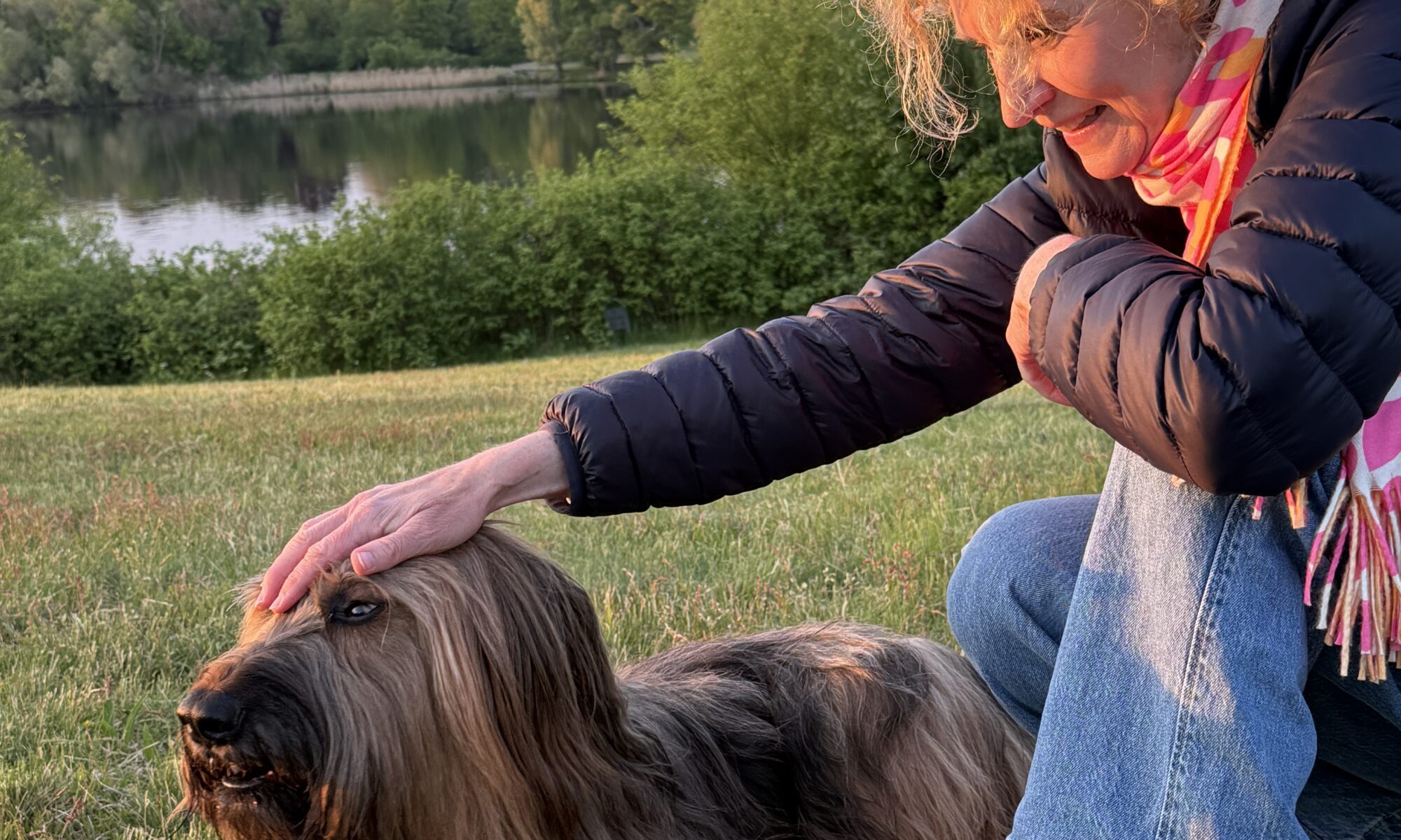 eine Frau kniet neben ihrwem Hund und streichelt ihn