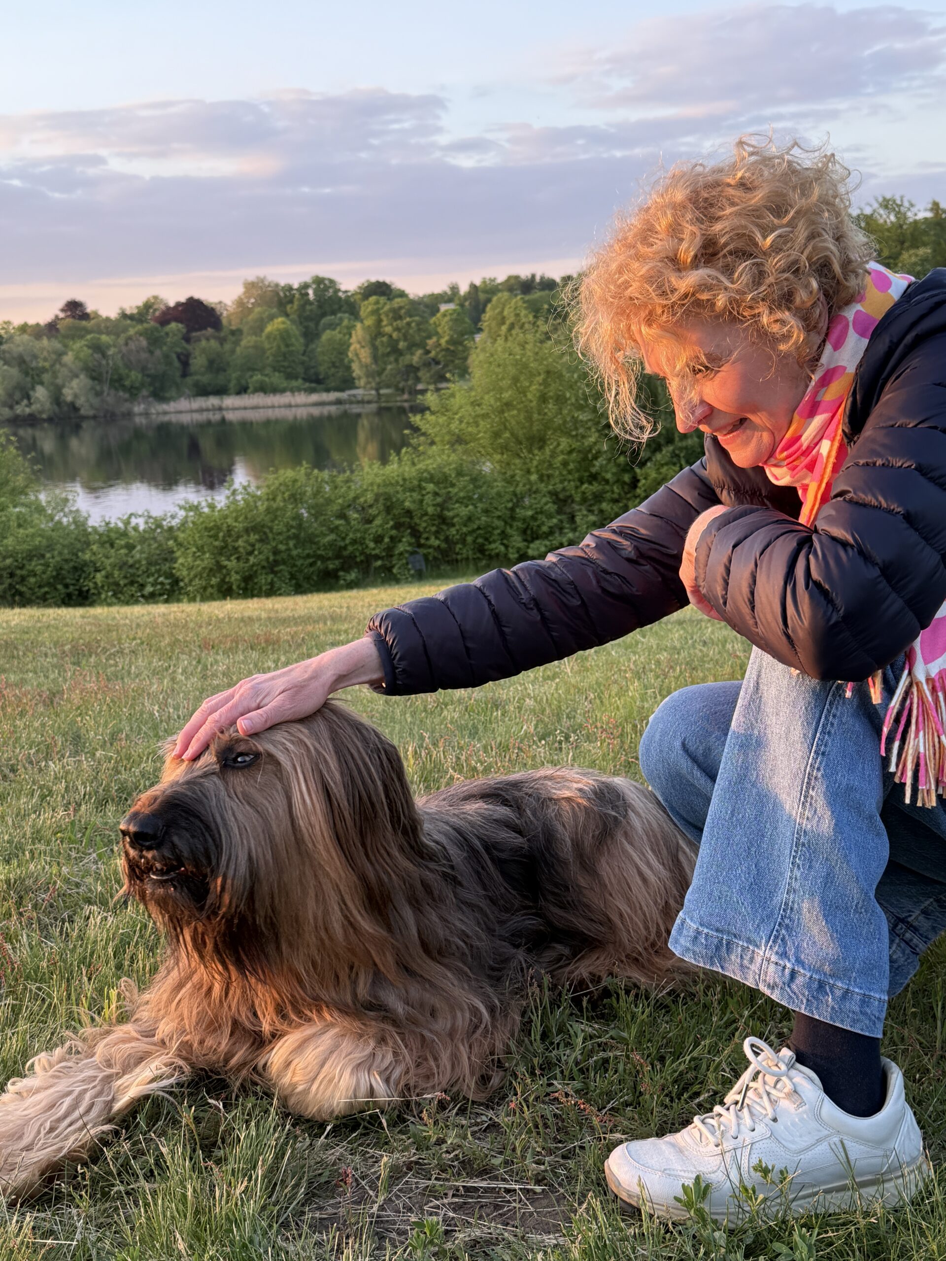 eine Frau kniet neben ihrwem Hund und streichelt ihn